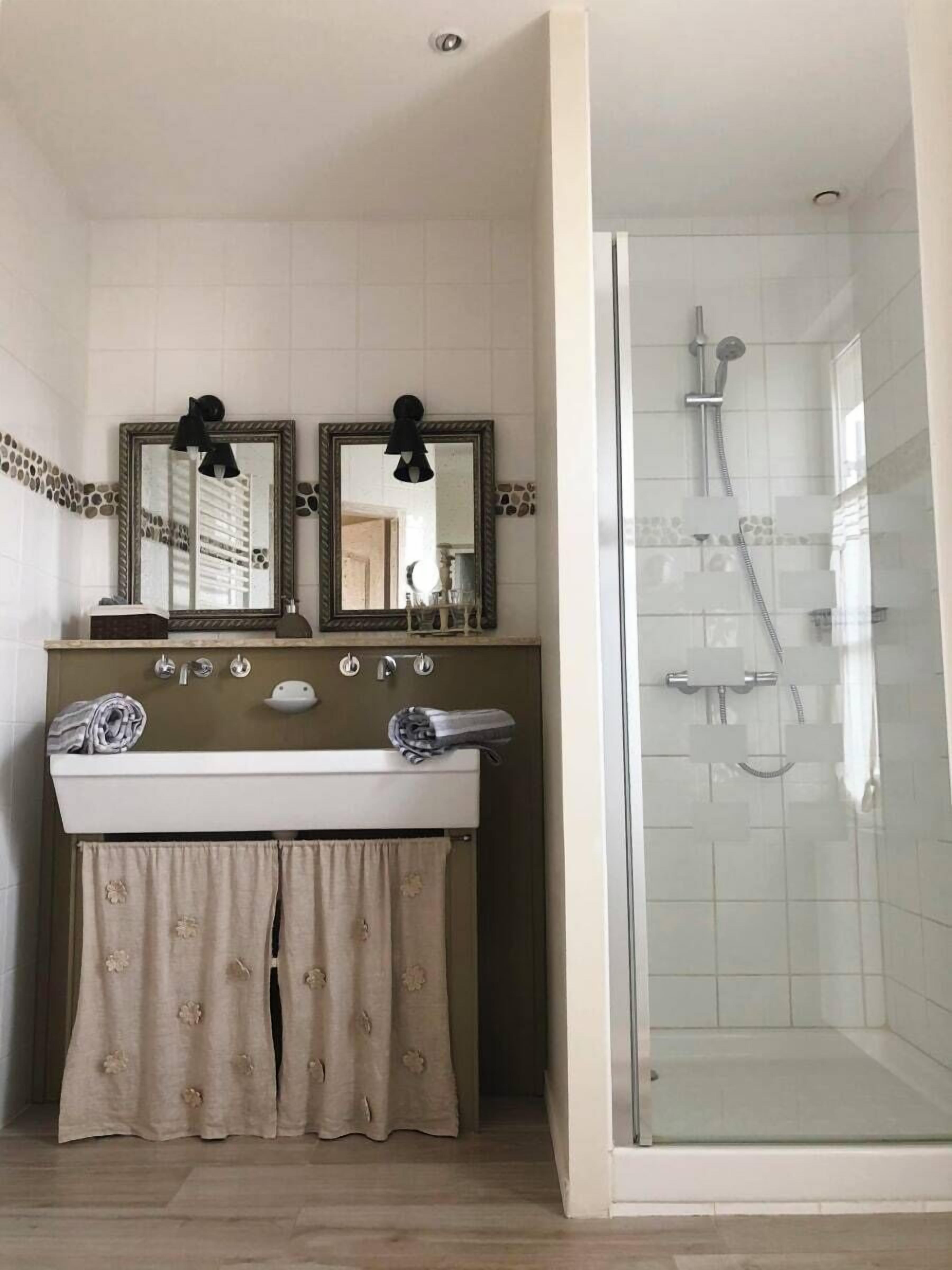 A bathroom with a double sink, two mirrors, a shower, and a glass-enclosed shower area.