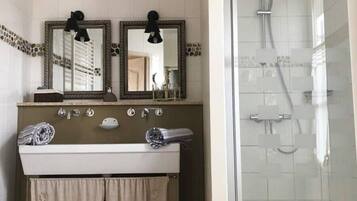 A bathroom with a double sink, two mirrors, a shower, and a glass-enclosed shower area.