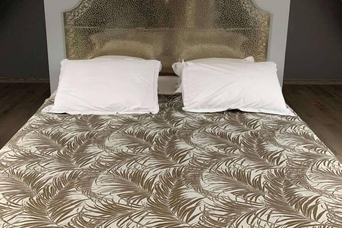 A bed with a leaf-patterned bedspread, a decorative headboard, and two white pillows.
