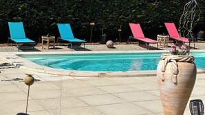 A pool area with lounge chairs, a decorative vase, and a potted plant. - Chambre d'Hôtes Ecole de Mathuna (Jaunay-Marigny)