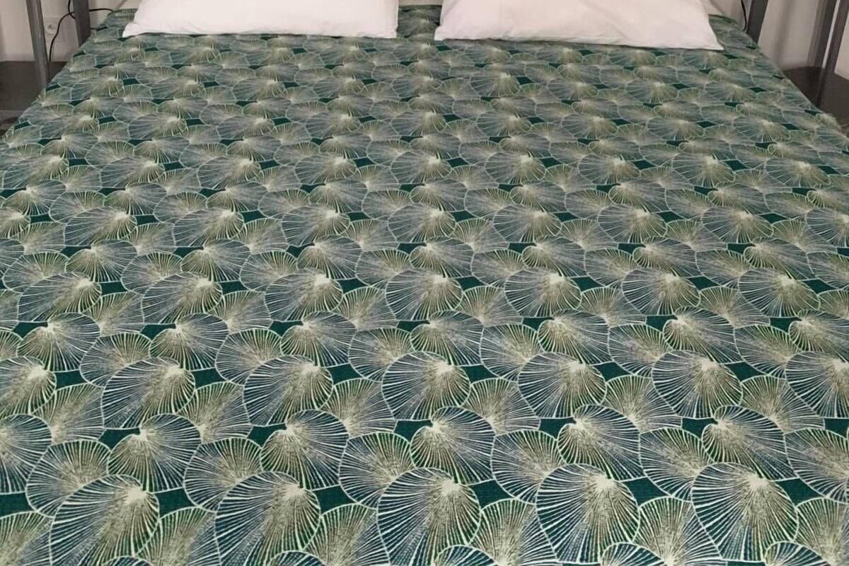 A bed with a green patterned bedspread, two white pillows, and a chalkboard headboard with writings.