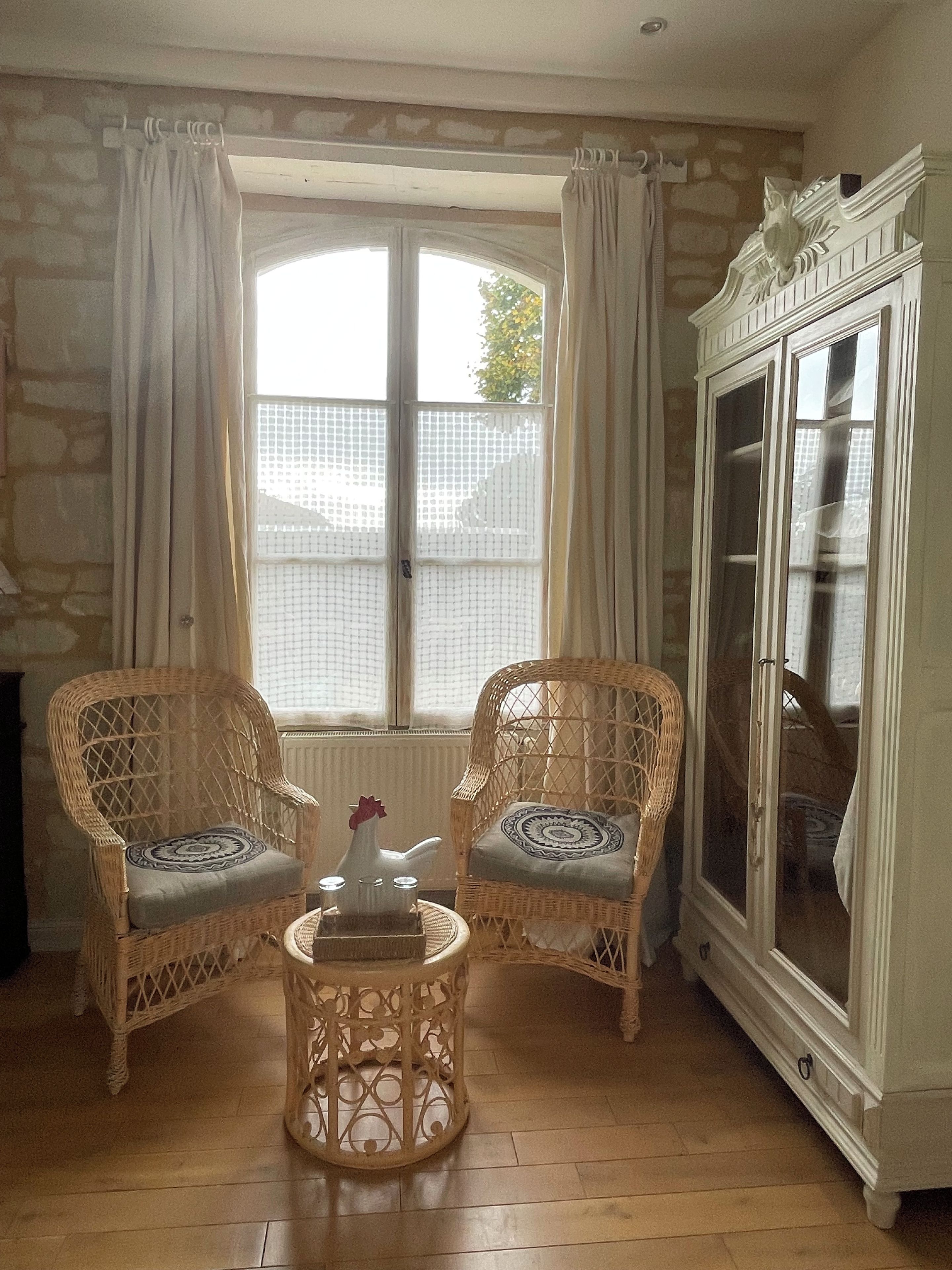 A room with two wicker chairs, a small round table with a vase, a cabinet, and a window with curtains.