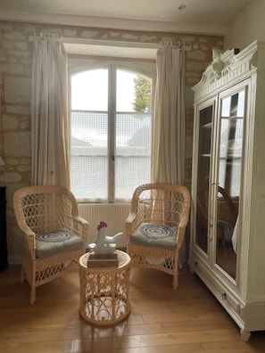 A room with two wicker chairs, a small round table with a vase, a cabinet, and a window with curtains. - Chambre d'Hôtes Ecole de Mathuna (Jaunay-Marigny)