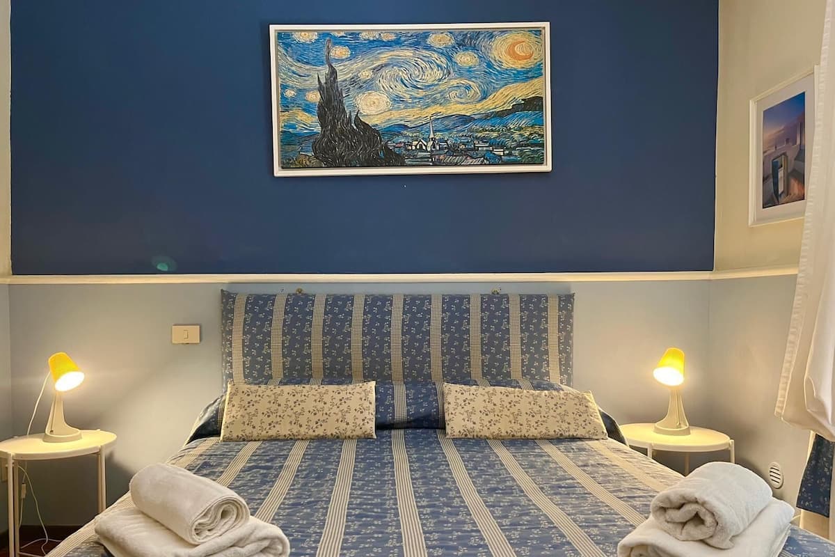 Una camera da letto con un letto, due abat-jour, un quadro appeso al muro e asciugamani sul letto.