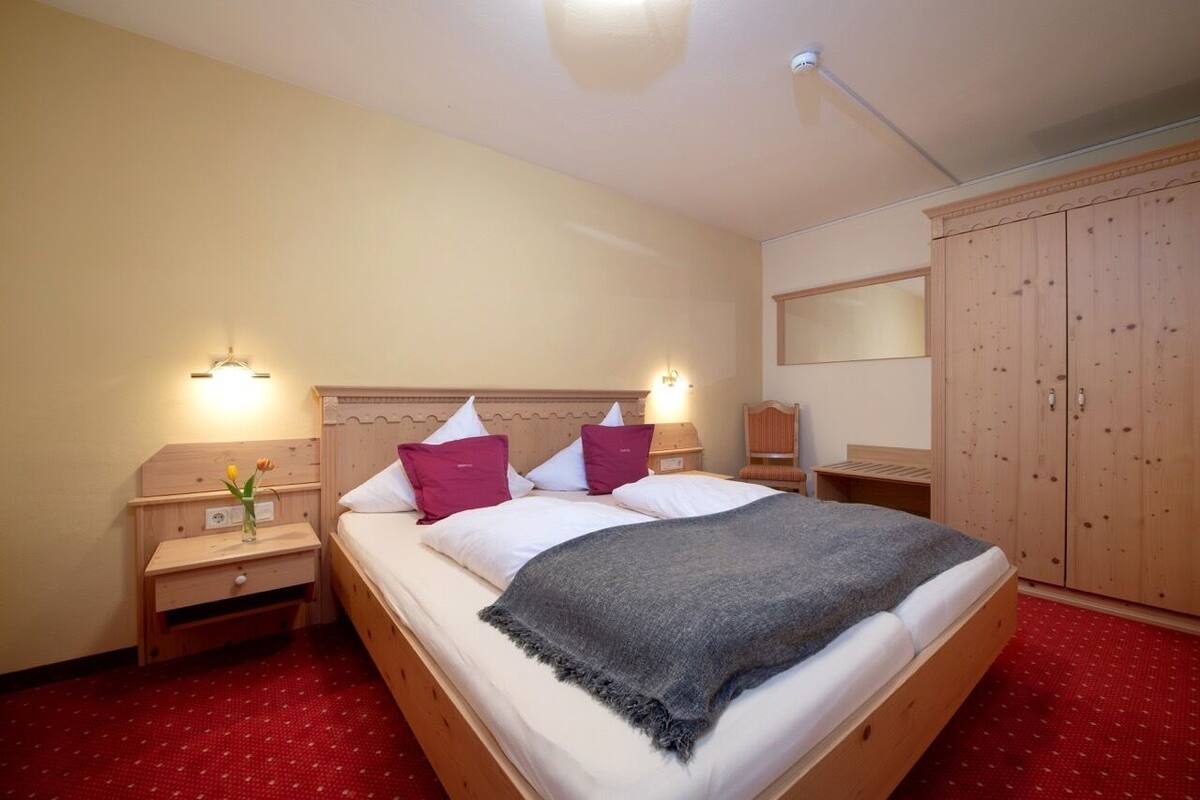 Een net opgemaakt bed met een grijze deken, houten hoofdbord en twee nachtlampjes.