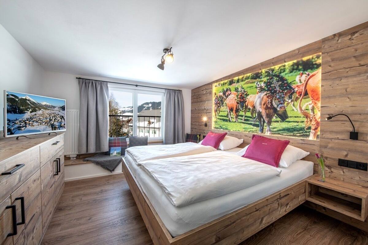 Een slaapkamer met een groot bed, een televisie, een houten dressoir en een schilderij van koeien aan de muur.
