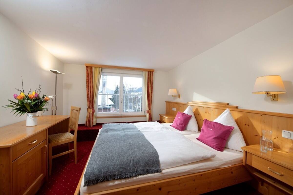 Een hotelkamer met een bed, nachtkastjes, een bureau, een stoel, een raam met gordijnen en een bloemenvaas.