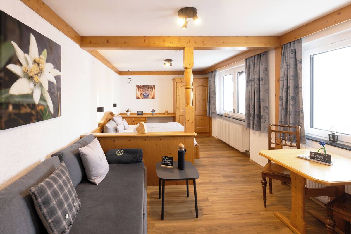 Een gezellige kamer met een houten plafond, een bank met kussens, een kleine tafel en een raam met gordijnen.