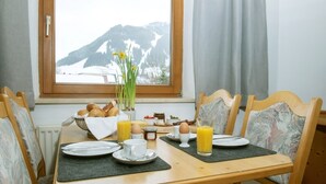 A breakfast table set with plates, cups, and a bowl of pastries, with a window view of mountains. - Käserstube Ferienwohnungen (Tannheim)