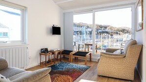 Ett modernt vardagsrum med utsikt över en småbåtshamn, en soffa, en fåtölj, ett litet bord och en tv som är monterad på väggen.