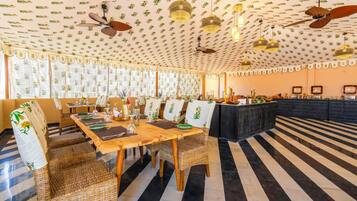 A dining area with a long wooden table, wicker chairs, and a patterned ceiling.