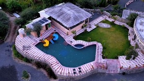 Ett flygbildsbild av ett semesterområde med en swimmingpool, en vattenrutschkana och en liten byggnad med ett halmtak.