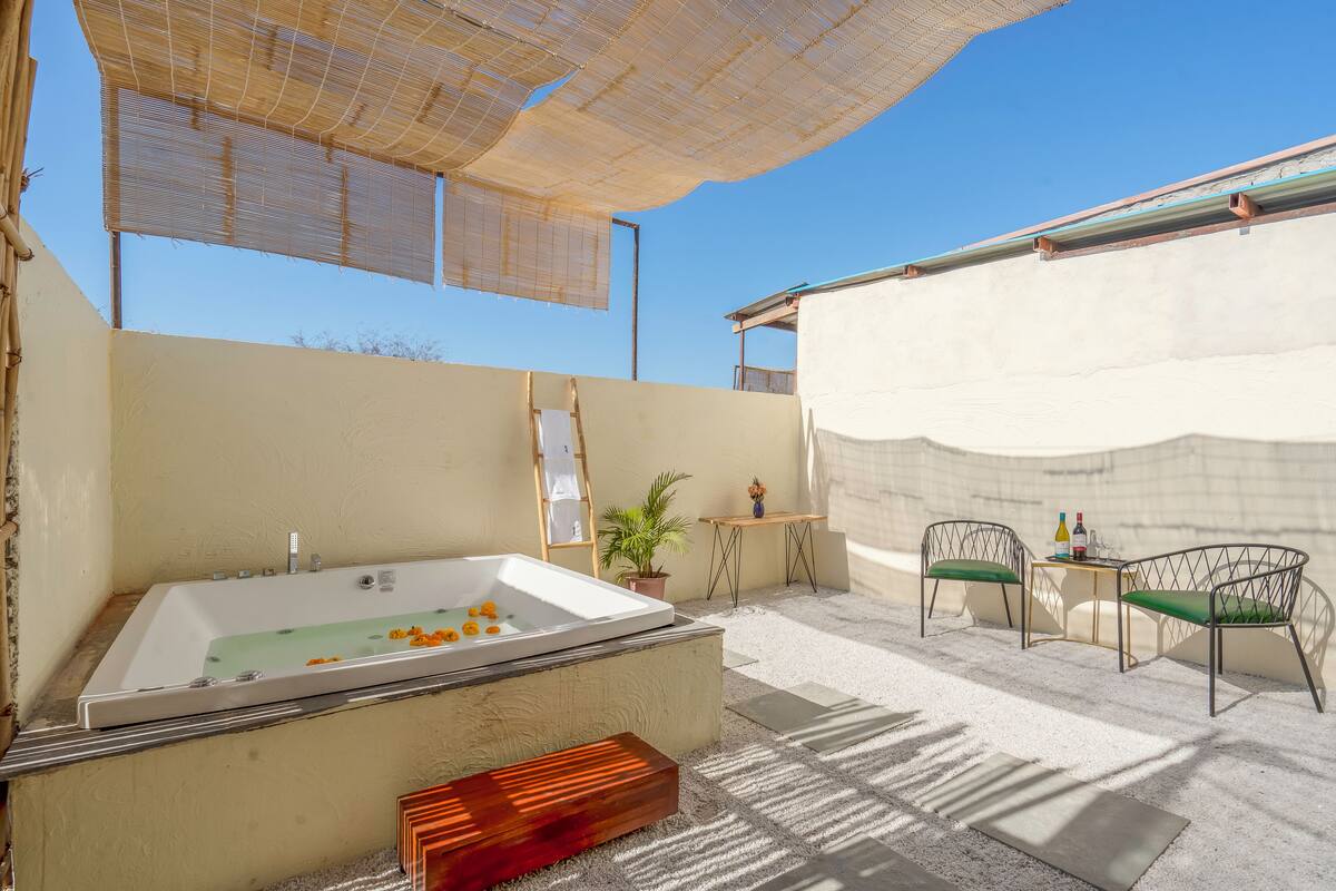 Un espace spa comprenant une grande baignoire, deux fauteuils, une petite table et une plante en pot.