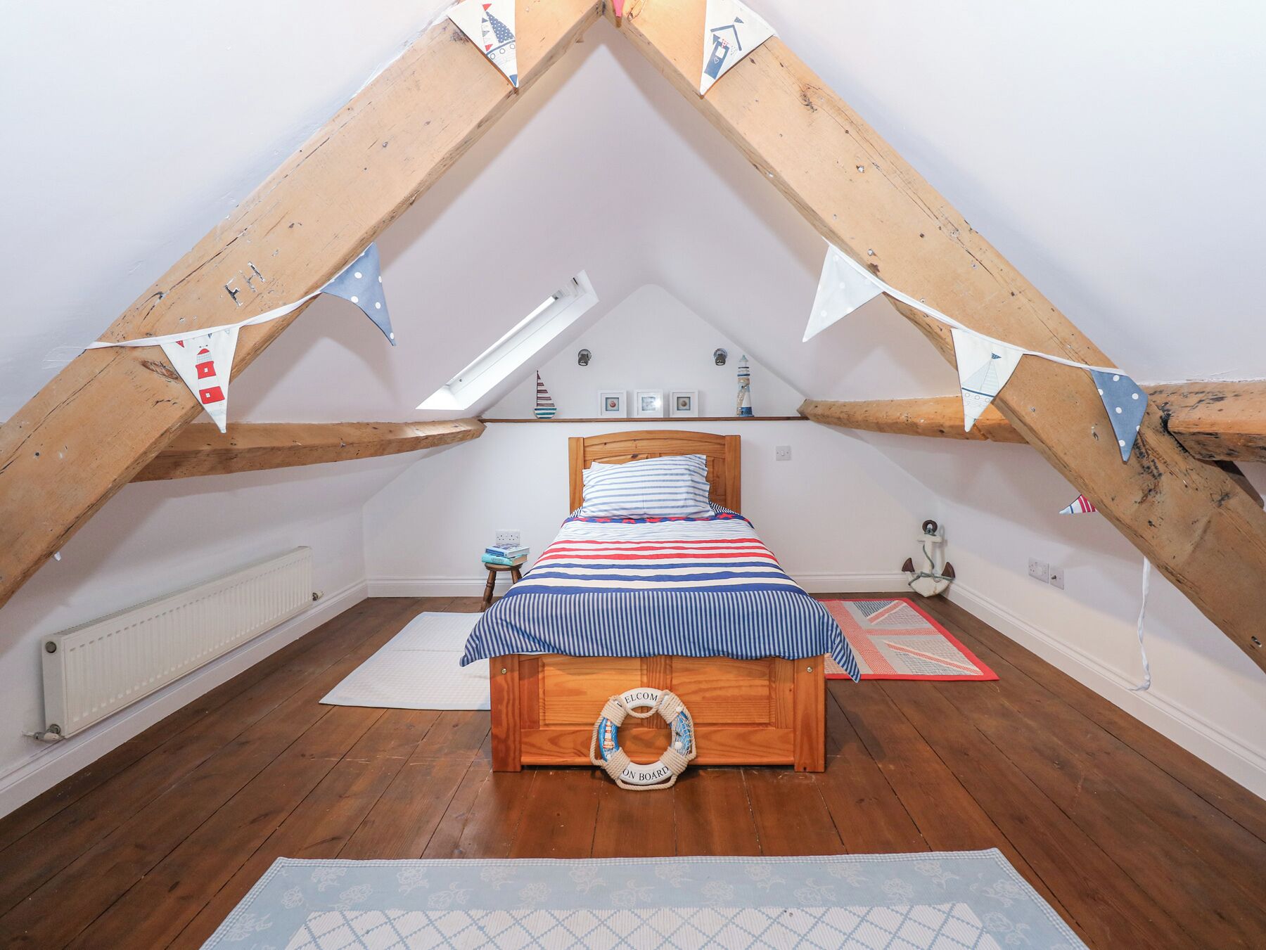 A cozy attic bedroom with a sloped ceiling, wooden beams, a bed with striped bedding, a small side table, and a decorative wall hanging.