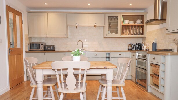 Una cocina con mesa y sillas de madera, microondas, fregadero y armarios.