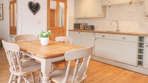 Una cocina compacta con armarios blancos, una mesa de comedor de madera y una planta en maceta.