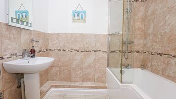 Un baño con lavamanos, espejo, ducha y paredes con azulejos.