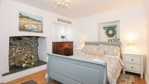 Un dormitorio con chimenea de piedra, una cama con cabecera, un aparador, una mesita de noche y una lámpara fijada a la pared.
