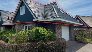 A modern house with a steeply pitched roof, a brick facade, and a white garage door. - Apartment in Sint Maartenszee Near Beach (Sint Maartensvlotbrug)