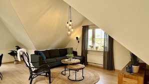 A cozy loft bedroom with a sloped ceiling, a dark green sofa, a wooden coffee table, a black chair, and a small wooden side table. - Apartment in Sint Maartenszee Near Beach (Sint Maartensvlotbrug)