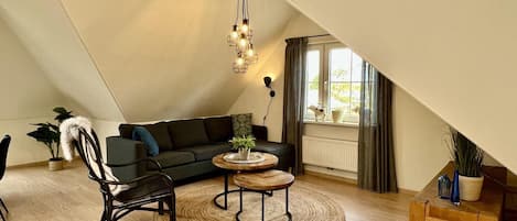 A cozy loft bedroom with a sloped ceiling, a dark green sofa, a wooden coffee table, a black chair, and a small wooden side table.