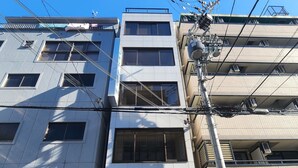 Um edifício de vários andares com uma persiana fechada no andar térreo, um elevador visível e varandas nos andares superiores.