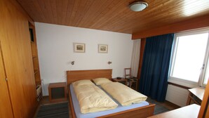 A wooden bed with two pillows, a bedside table, a small cabinet, and a window with curtains.