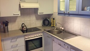 A compact kitchen with white cabinets, a stove, oven, dishwasher, and a sink.