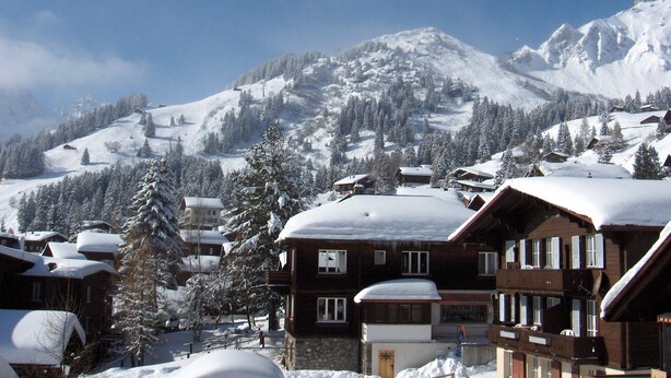 A snow-covered mountain village with wooden buildings and snow-covered trees.