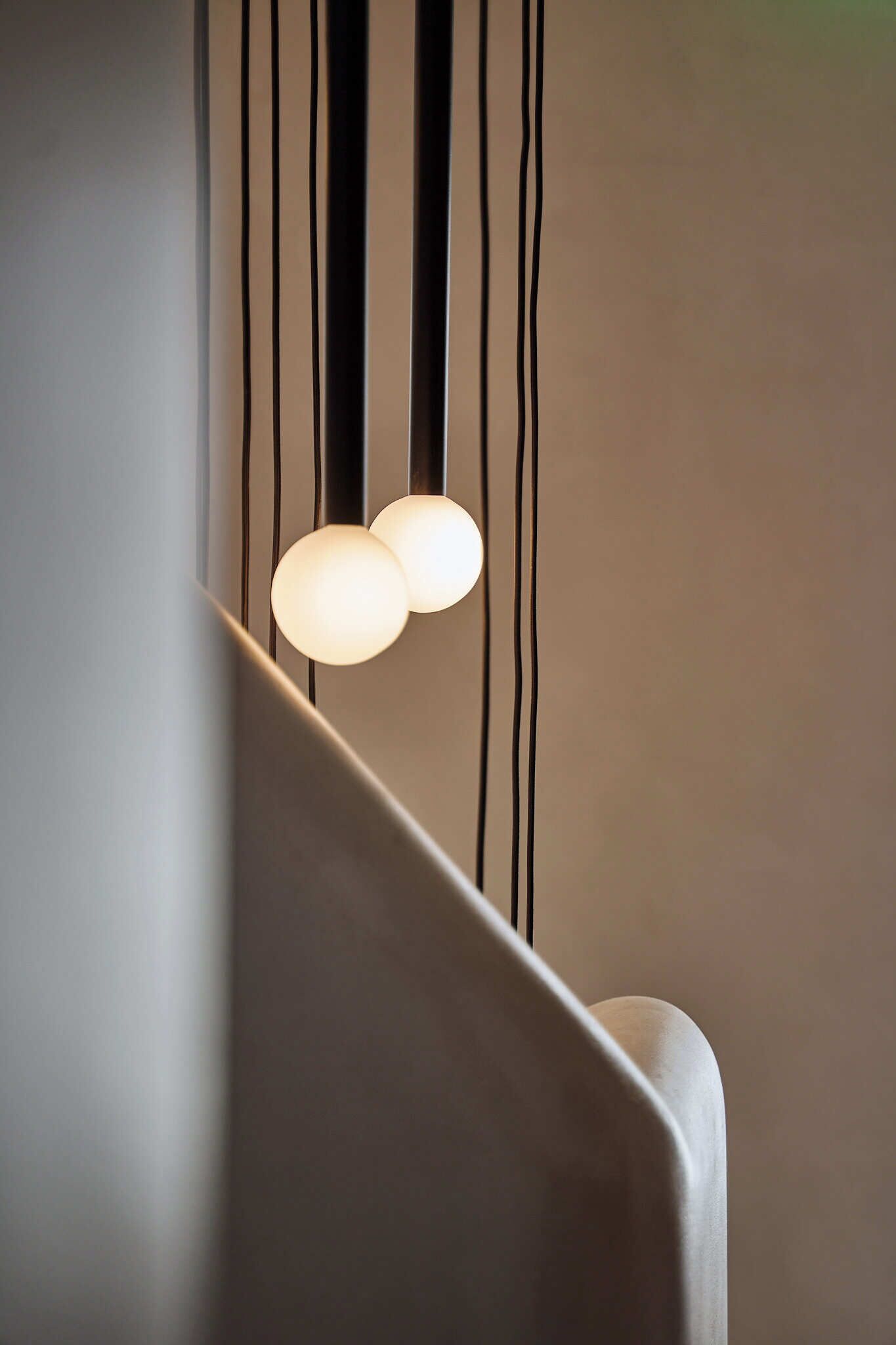 Un intérieur moderne avec un mur aux lignes épurées et incurvées, ainsi qu’un luminaire suspendu doté de deux ampoules sphériques.