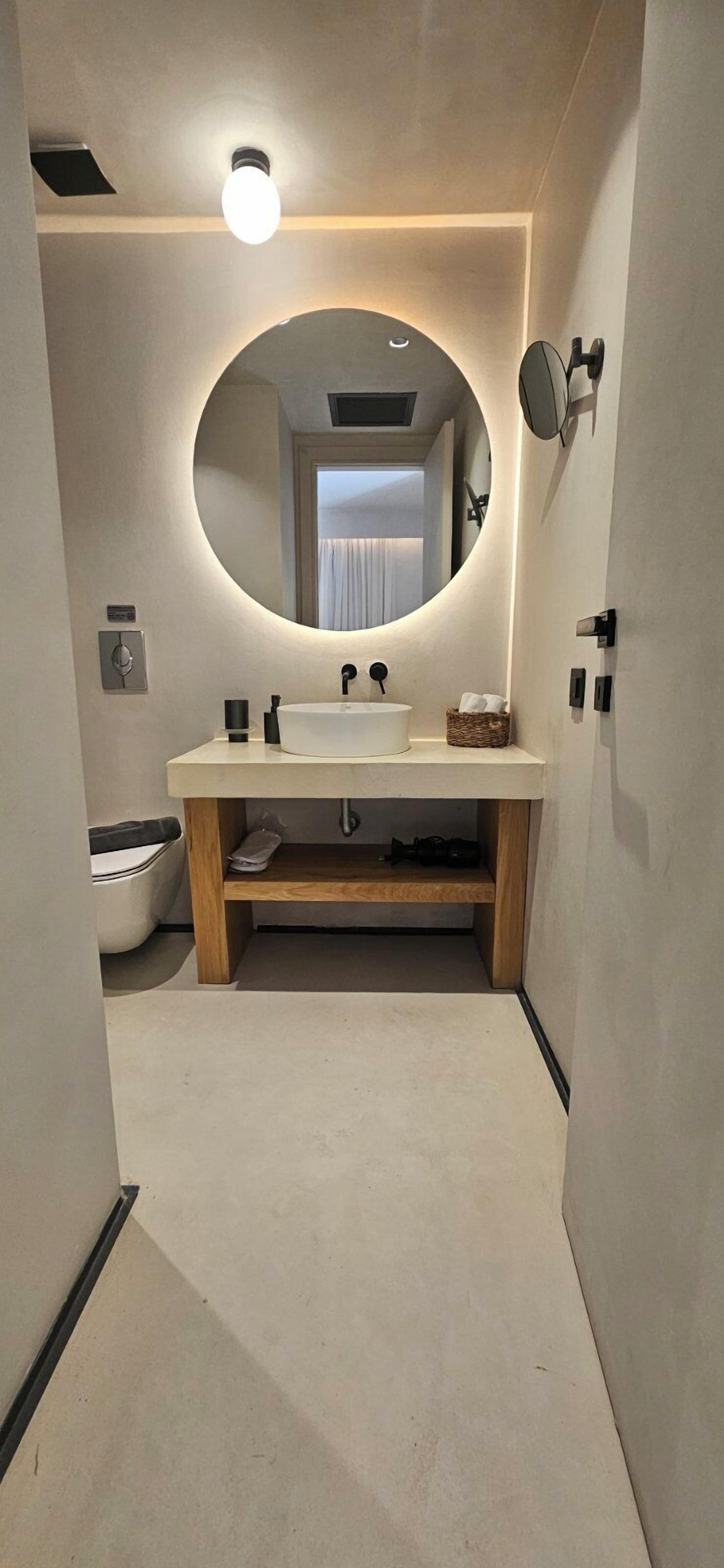 A modern bathroom with a round mirror, a sink, and a toilet.