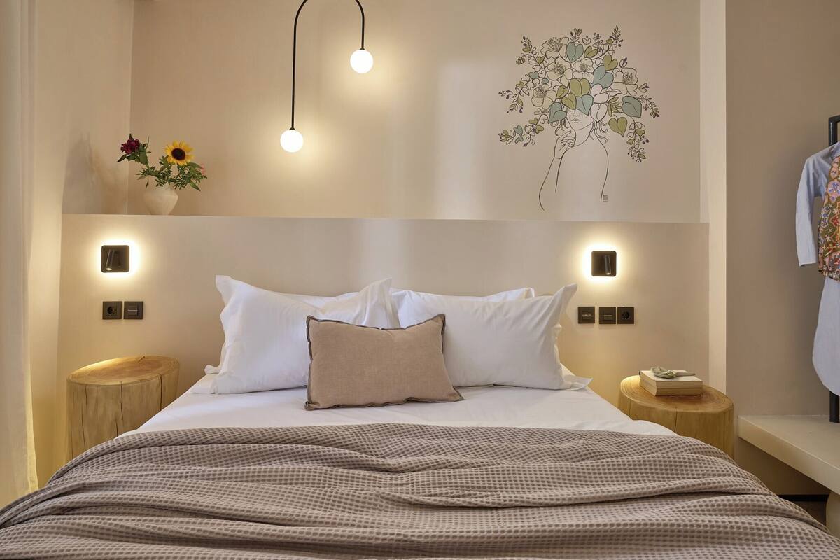 A neatly made bed with a patterned blanket, bedside tables with books, and wall-mounted lights.