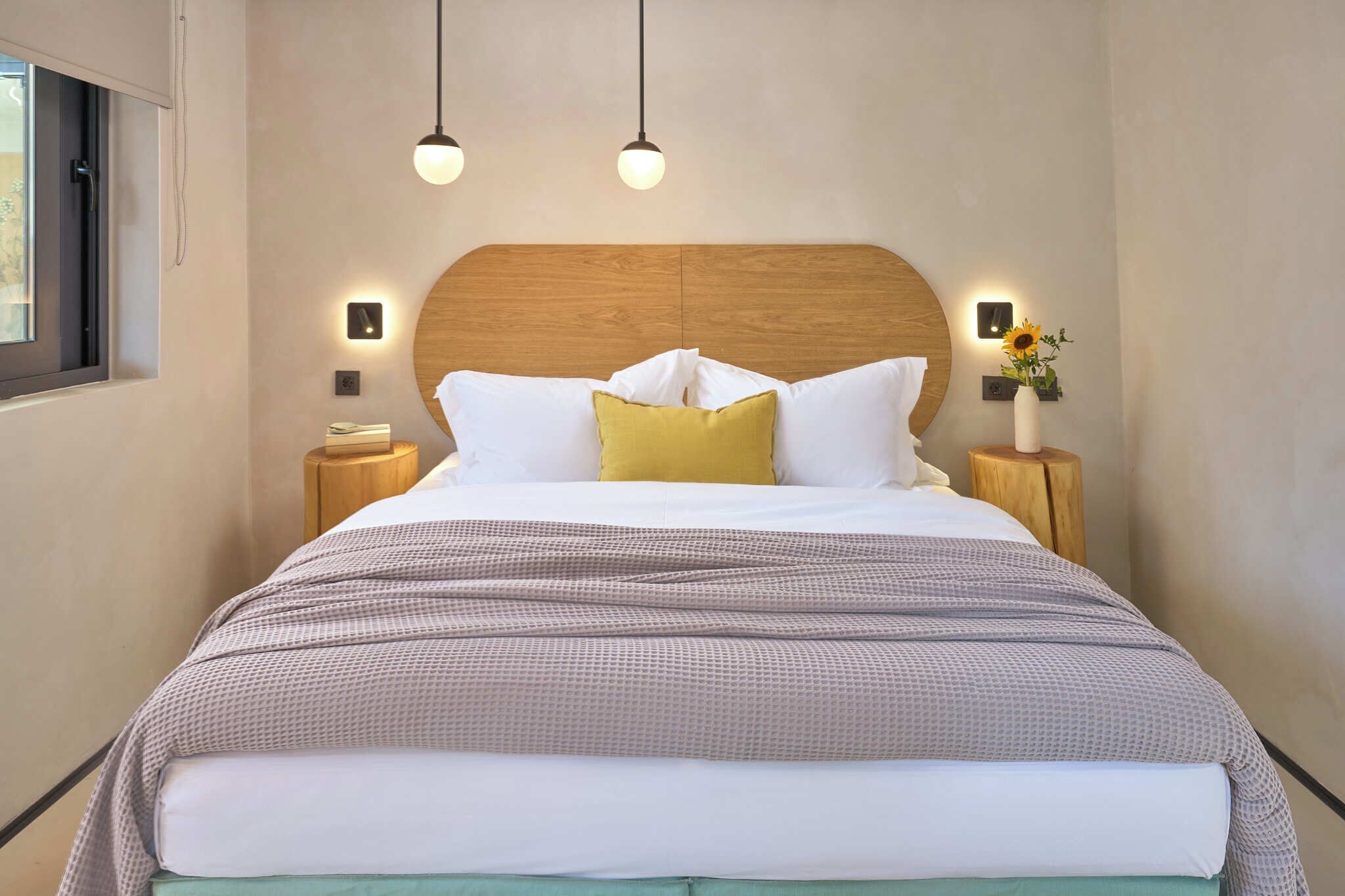 A neatly made bed with a wooden headboard, two bedside lamps, and a vase with flowers on a nightstand.