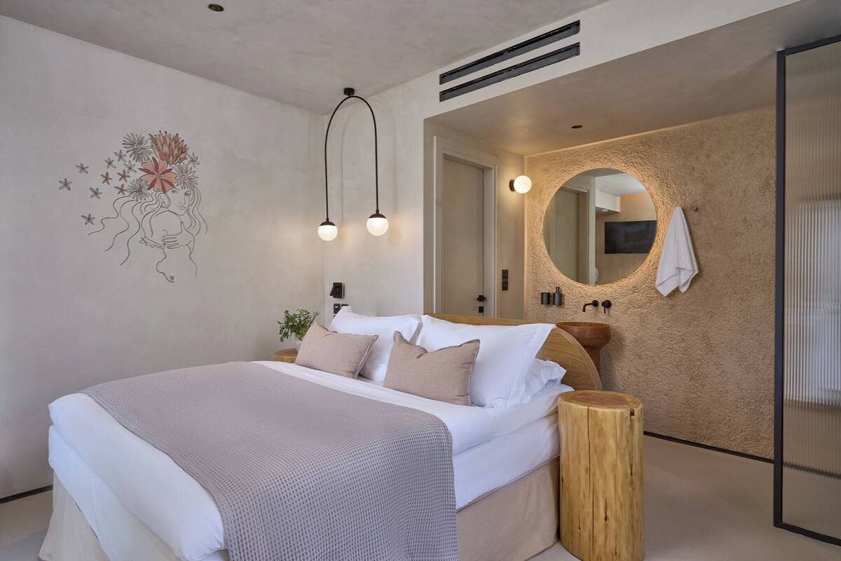 A modern bedroom with a large bed, a wooden bedside table, a round mirror, and a wall-mounted light fixture.