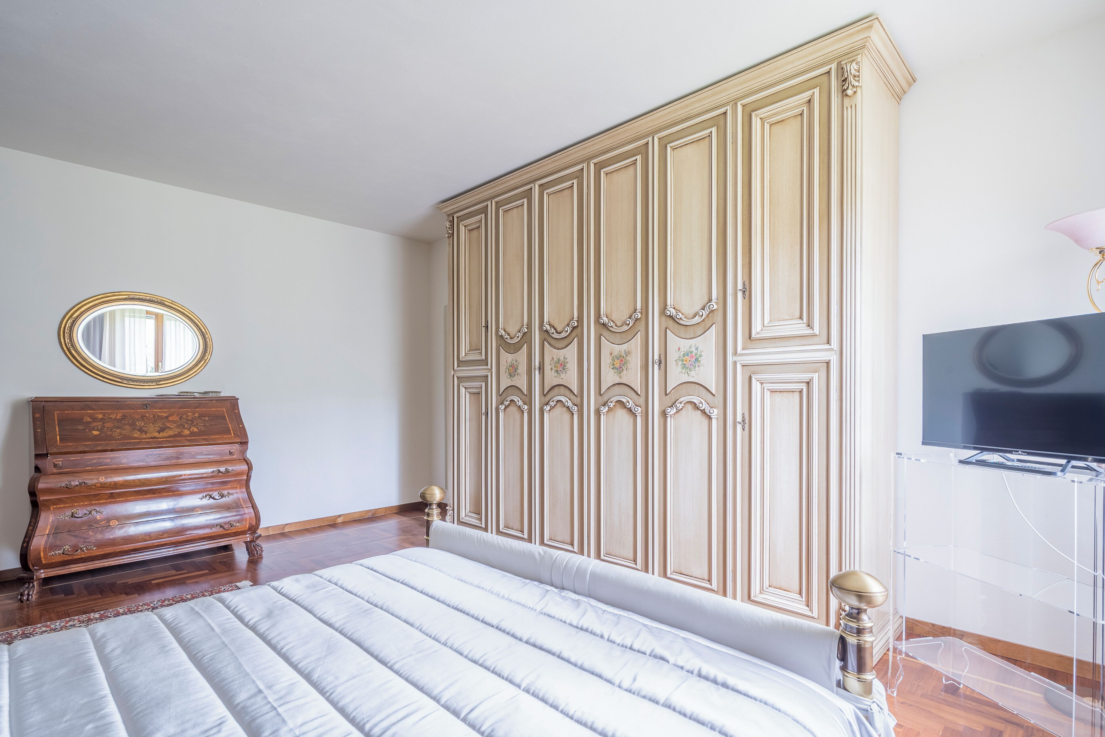 Une chambre à coucher avec un grand lit, une commode en bois, une armoire et un téléviseur.