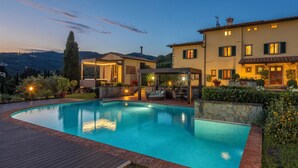 Una piscina circondata da un solarium in legno, con un muro in pietra e piante in vaso.