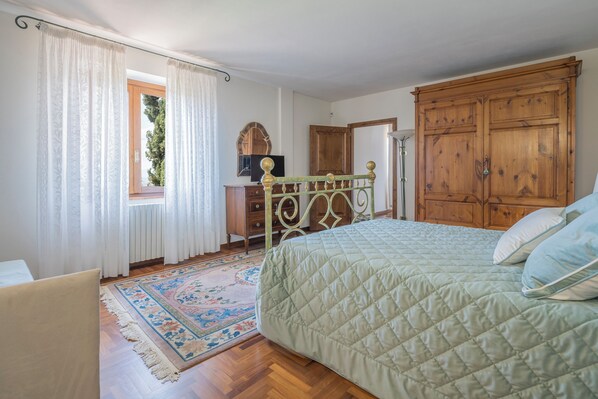 Une chambre à coucher avec un lit, une armoire en bois, une commode et une fenêtre avec des rideaux.