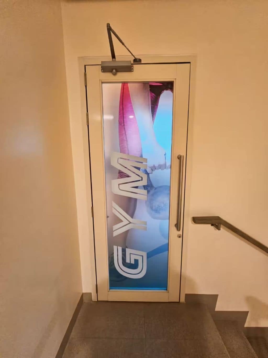 A door with a frosted glass panel displaying the word "GYM" and a partial view of a staircase.