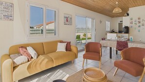 Ein modernes Wohnzimmer mit einer Couch, Sesseln, einem Esstisch und einer Küchenzeile.