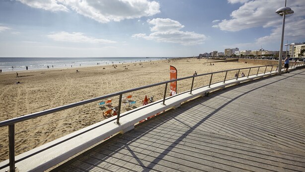 Ein Strand mit einer Holzpromenade, Sonnenschirmen und einer Flagge.