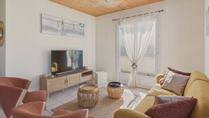 Ein Wohnzimmer mit Holzboden, einem Fernseher auf einer Holzkommode, einem Sofa und einem Fenster mit Vorhängen.