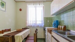 A compact kitchen with a dining table and chairs, a window with sheer curtains, and basic kitchen appliances.