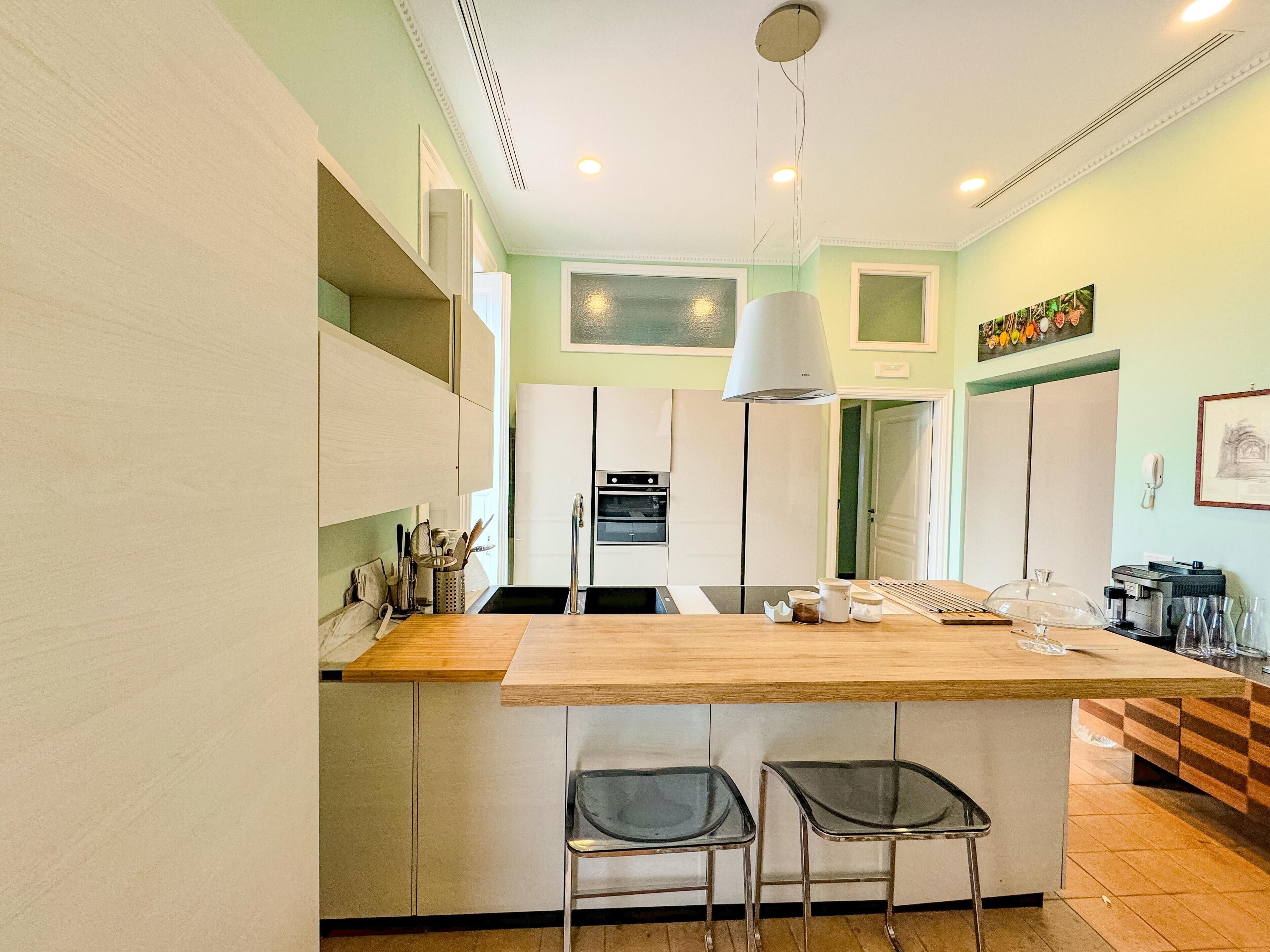 A modern kitchen with a central island, two bar stools, and a hanging light fixture.