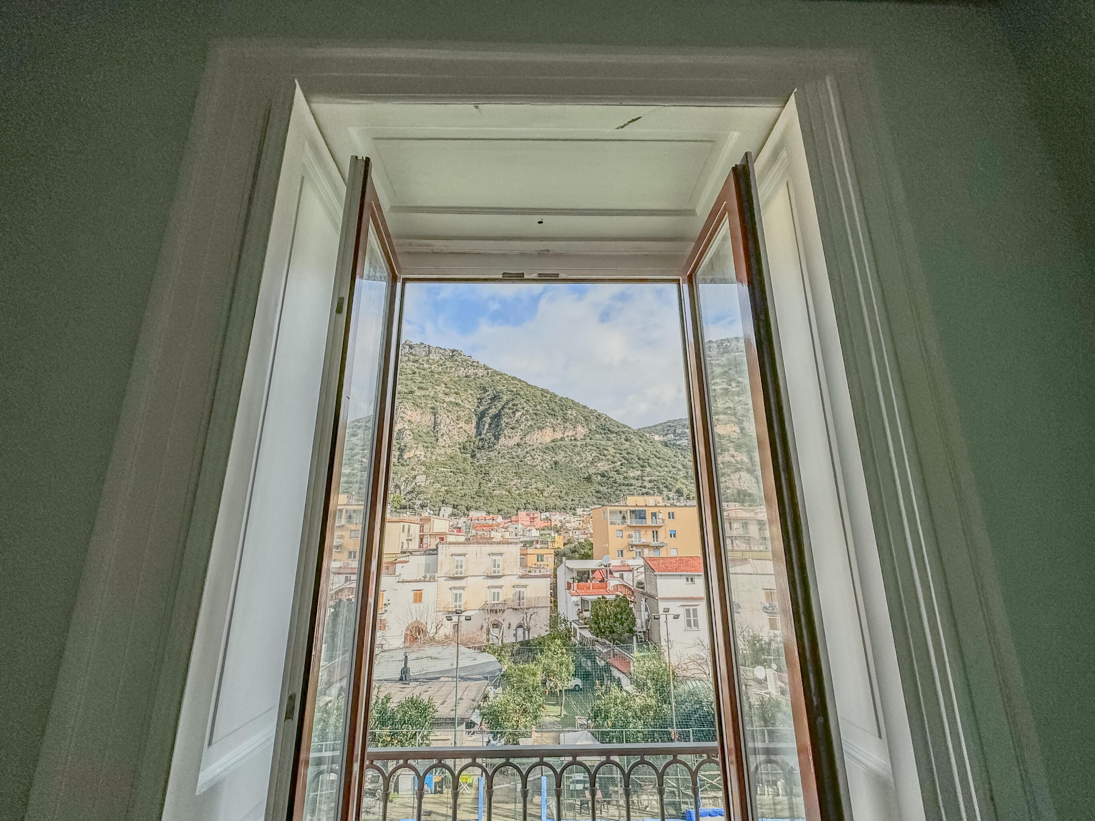 A view through a window of a building with a balcony, a mountain in the background, and a clear sky.