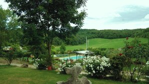 Een weelderige tuin met een stenen beeld, een zwembad en een prieel.