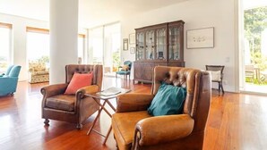 A spacious living room with leather armchairs, a wooden cabinet, and large windows.