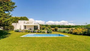 A modern house with a swimming pool, surrounded by well-maintained lawns and a variety of plants.
