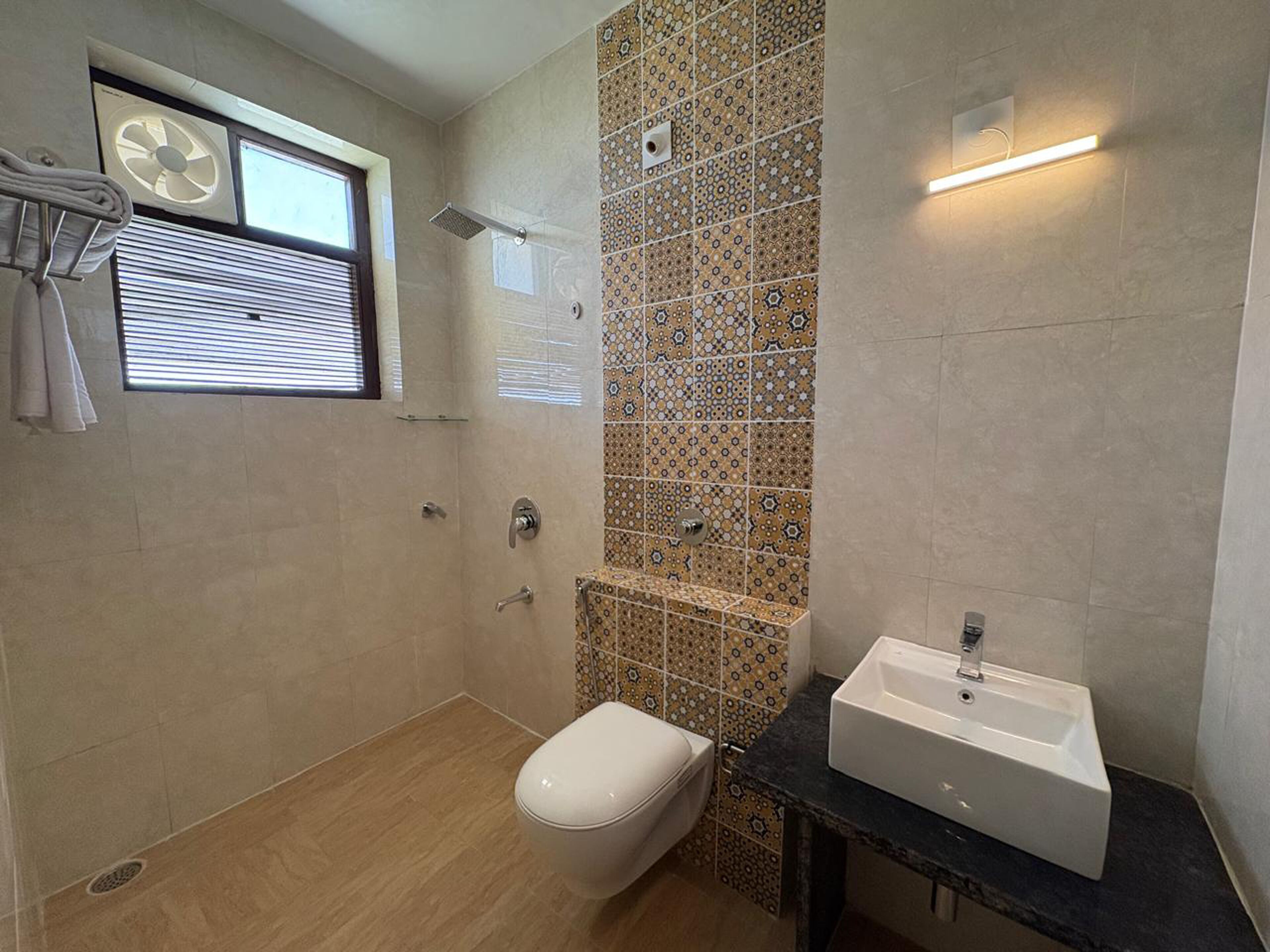 A bathroom with a toilet, sink, shower, and a window with blinds.