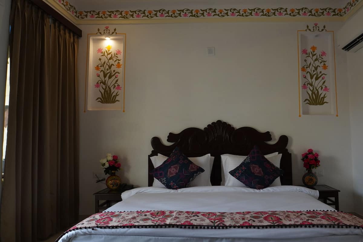 Un dormitorio con cabecera de madera, colcha con estampado floral, dos mesitas de noche con jarrones de flores y paneles decorativos en la pared.