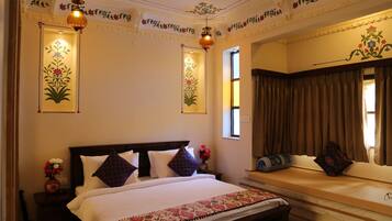 A well-lit bedroom with a large bed, a bedside table with a vase of flowers, and a window with curtains.